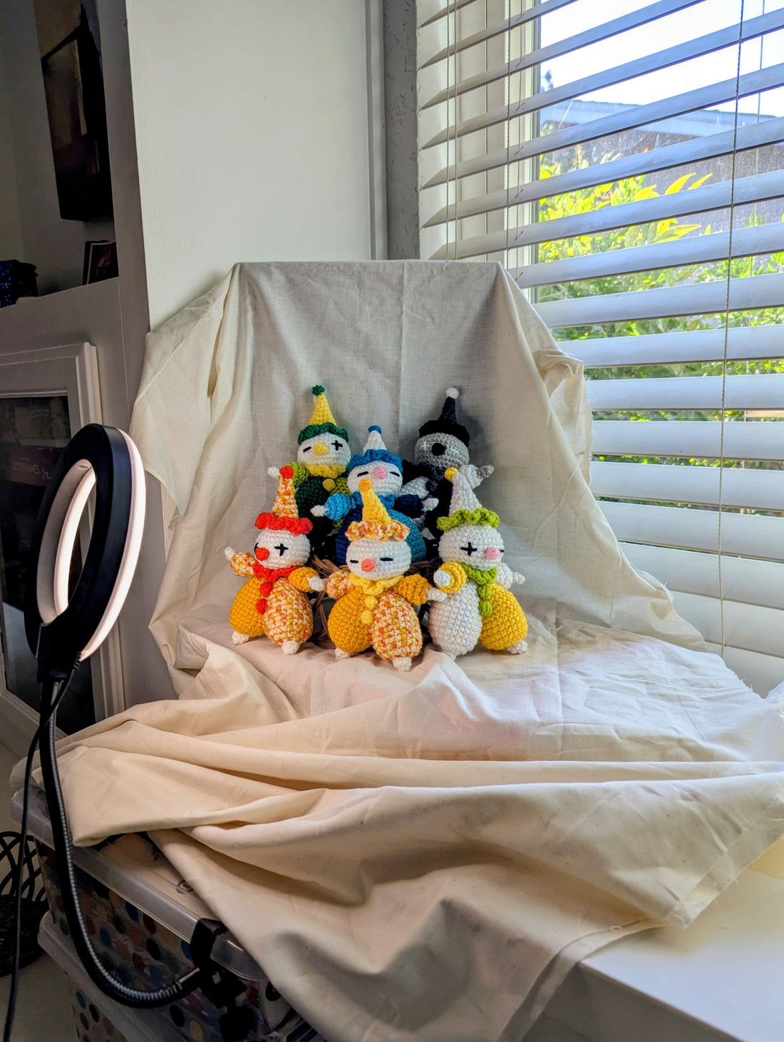 Six colorful crocheted clowns positioned on a beige backdrop for a photoshoot