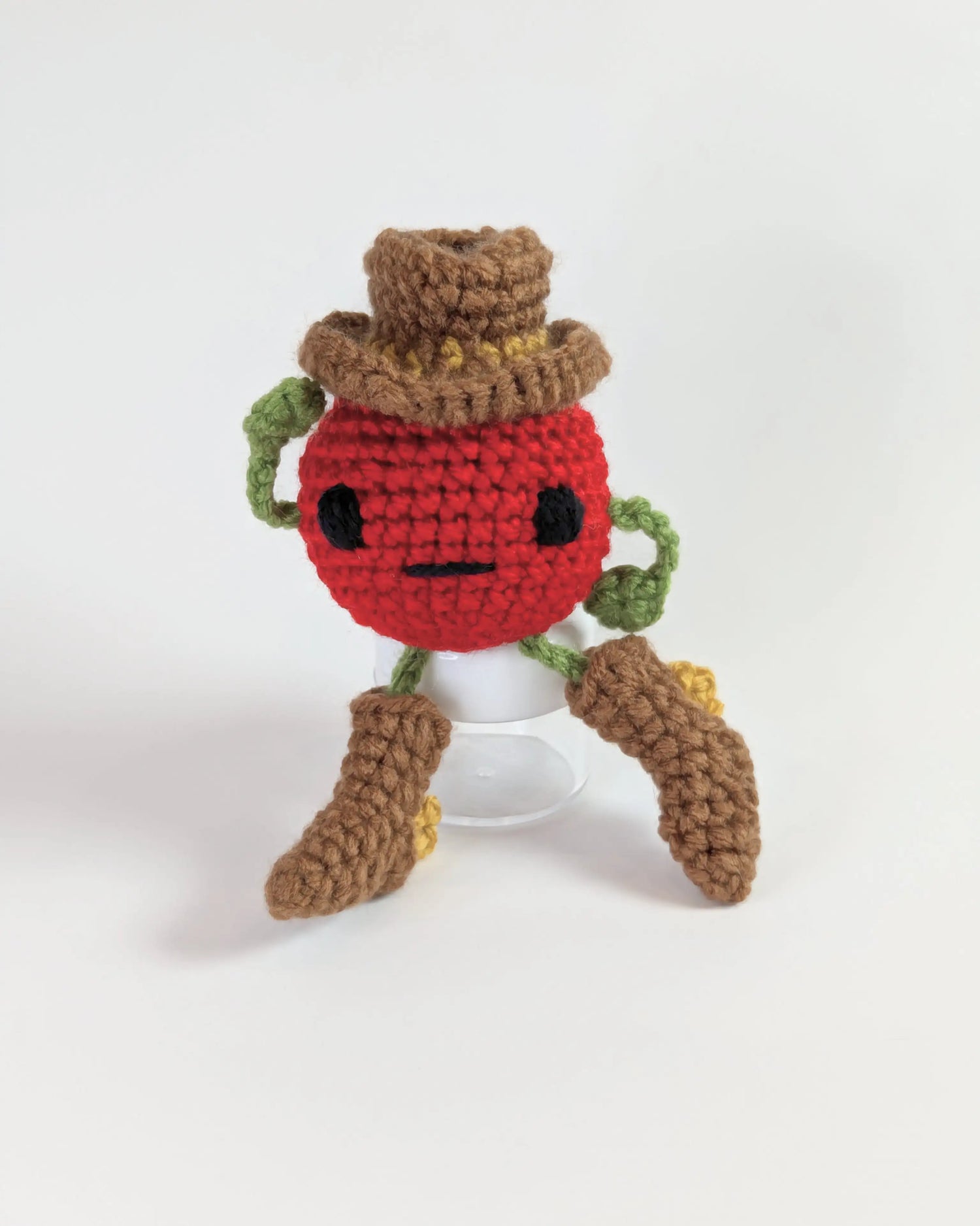 A crocheted soft toy in the shape of a cartoon tomato wearing a cowboy hat and cowboy boots