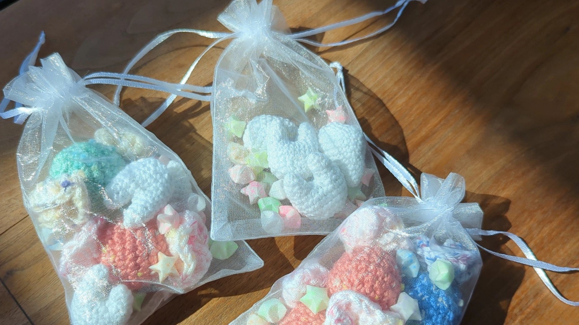 three organza bags holding crocheted soft toys of teeth and candy, as well as paper stars