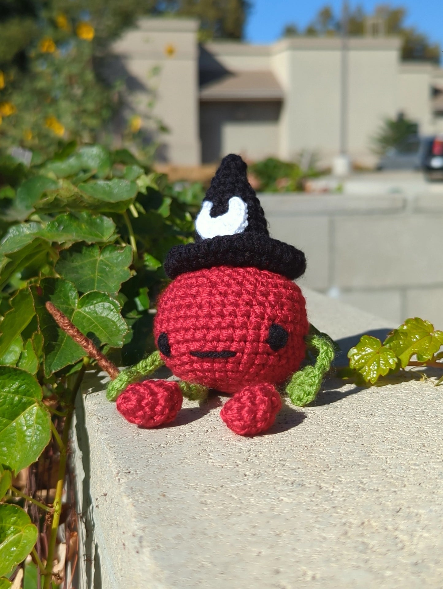 crocheted soft toy of a cartoon tomato wearing a witch hat and holding a wand