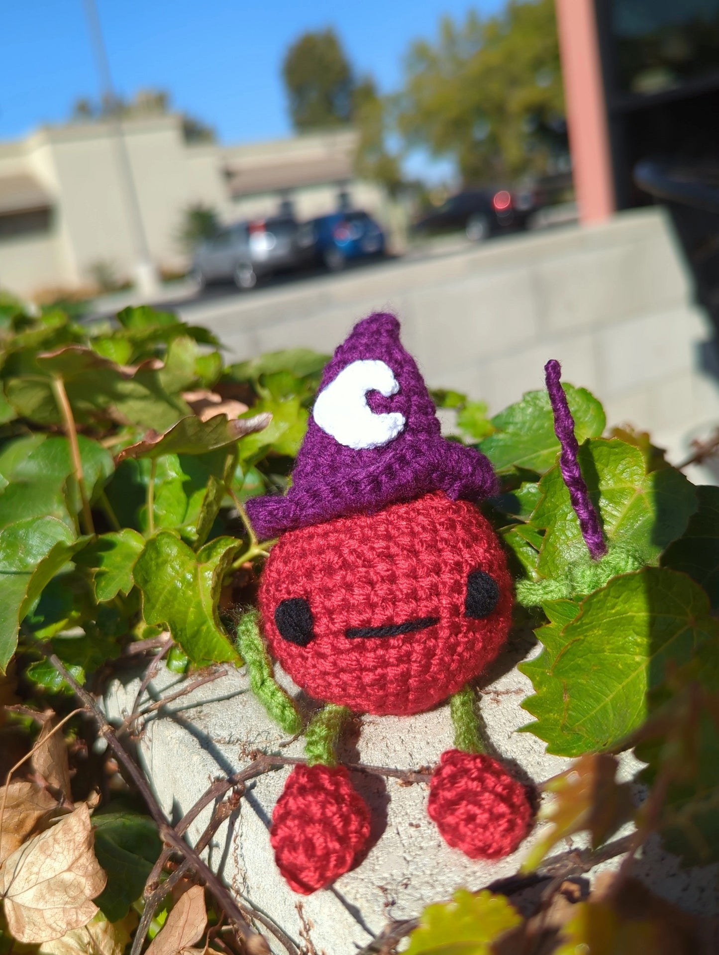 crocheted soft toy of a cartoon tomato wearing a witch hat and holding a wand