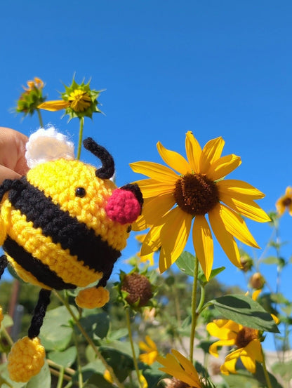 Crocheted soft toy of a cartoon bumble bee against a sunny backdrop