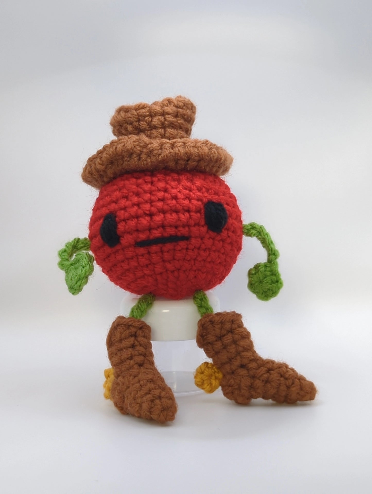 Crocheted soft toy of a cartoon tomato dressed like a cowboy against a white background