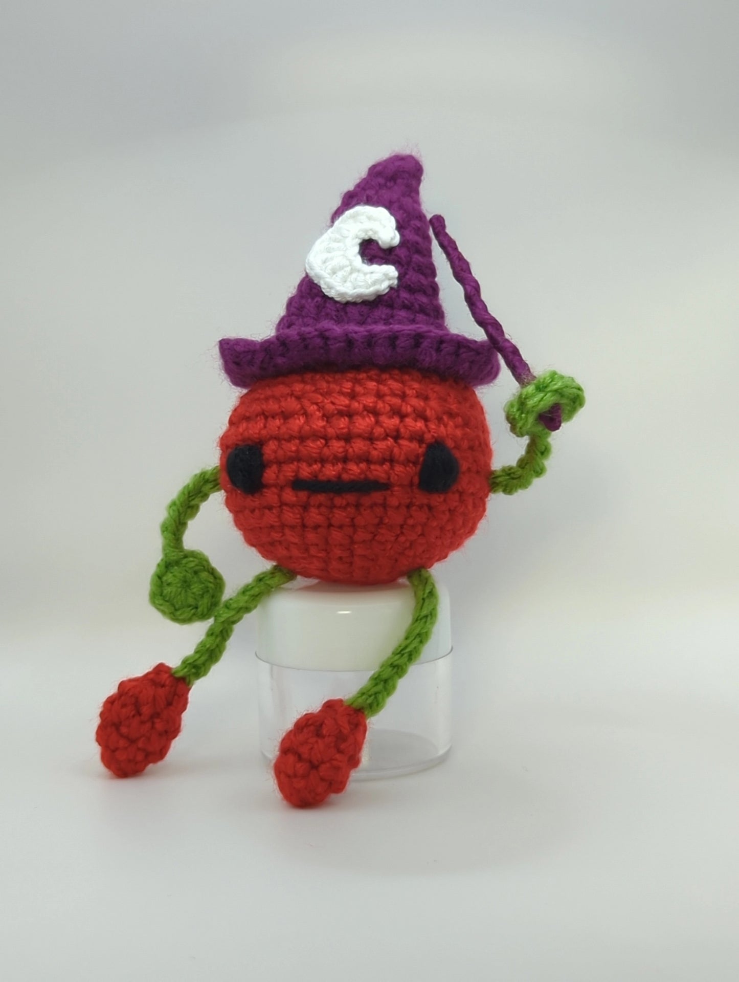 crocheted soft toy of a cartoon tomato wearing a witch hat and holding a wand