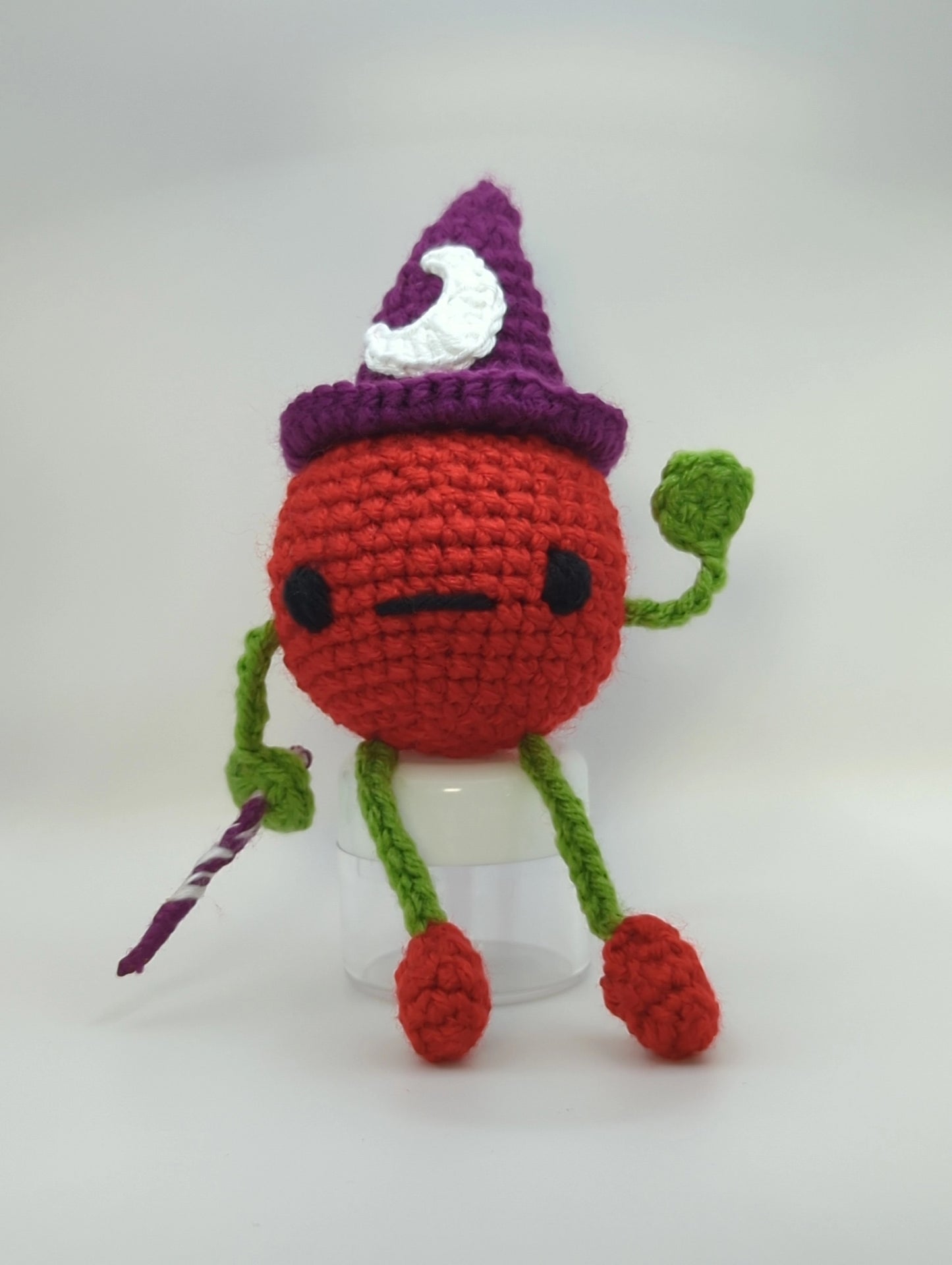 crocheted soft toy of a cartoon tomato wearing a witch hat and holding a wand