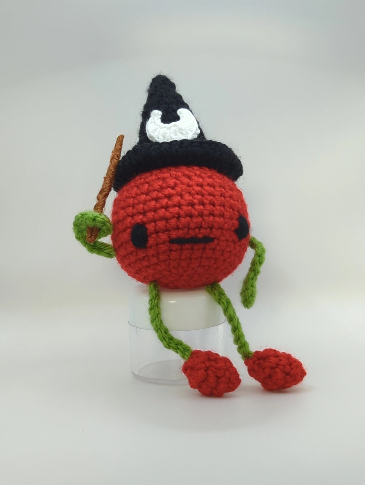 crocheted soft toy of a cartoon tomato wearing a witch hat and holding a wand