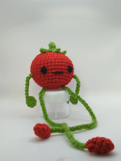 Crocheted soft toy of a cartoon tomato with very long legs sitting against a white backdrop