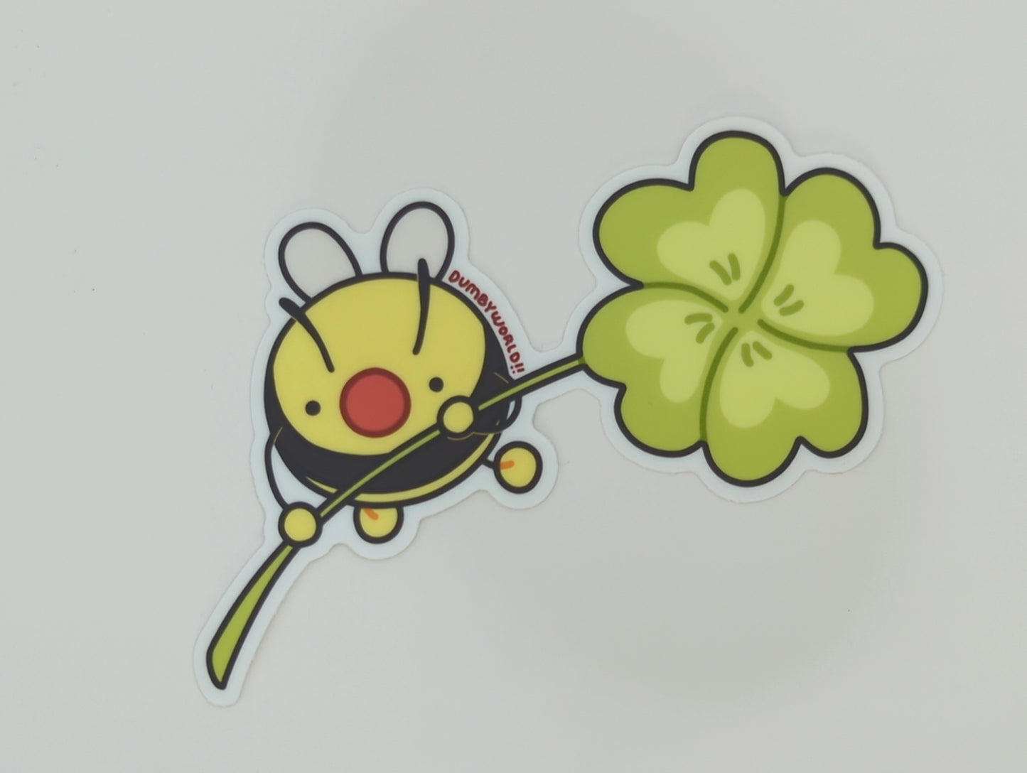 a sticker of a cartoon bumble bee holding a four-leafed clover