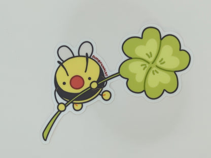 a sticker of a cartoon bumble bee holding a four-leafed clover